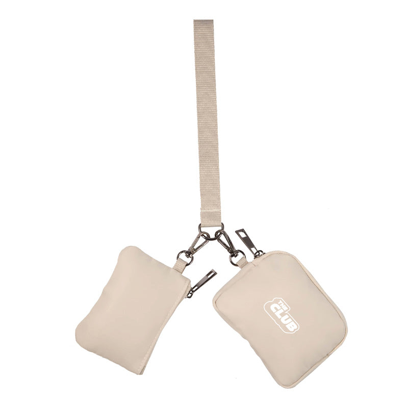 Beige dual-pouch wristlet with metal clips and a short strap, featuring ‘The Club’ logo on one of the zippered pouches.